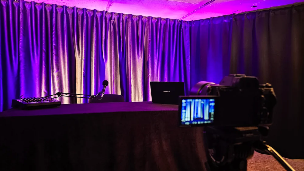 Sānskats video podkāstu studijai vienai personai ar kameru un violetu fonu.